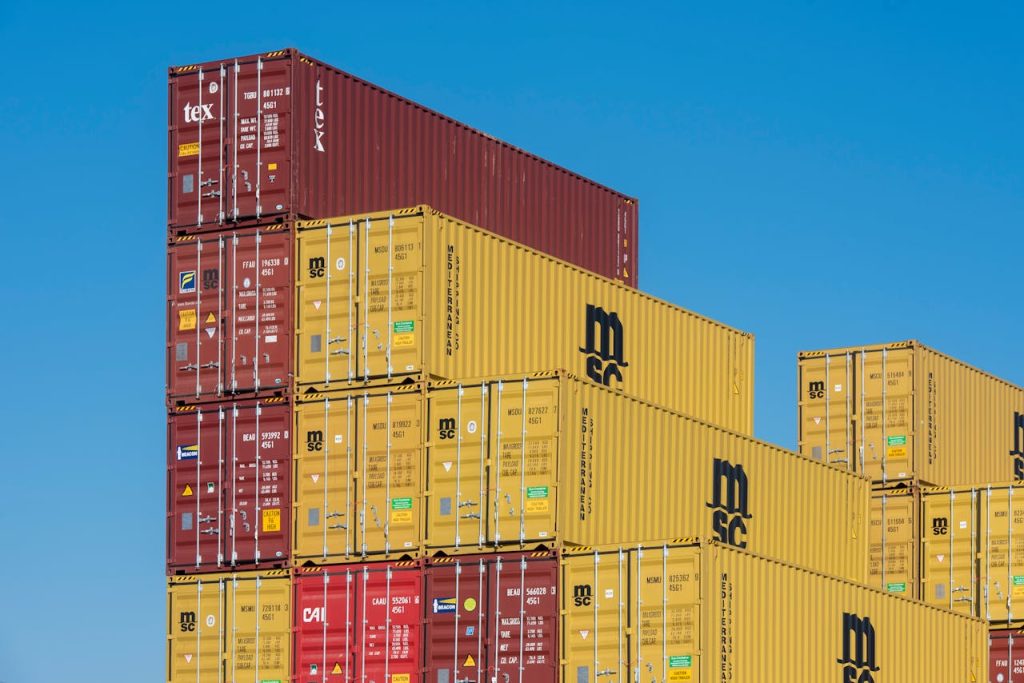 Colorful shipping containers stacked high under a clear blue sky, displaying industrial logistics.